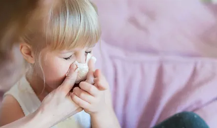 Una madre ayudando a su hija a sonarse la nariz con un pañuelo de papel