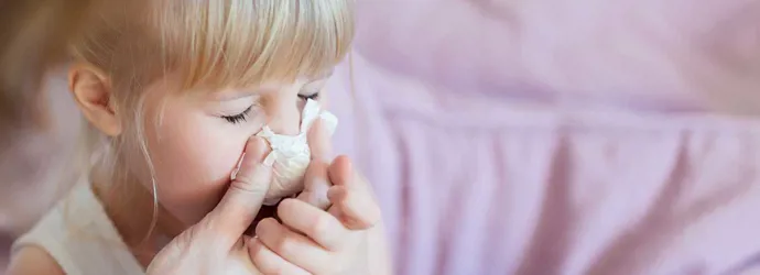 Una madre ayudando a su hija a sonarse la nariz con un pañuelo de papel