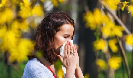 Una mujer joven estornudando en un pañuelo en un campo lleno de flores silvestres con una alta concentración de polen