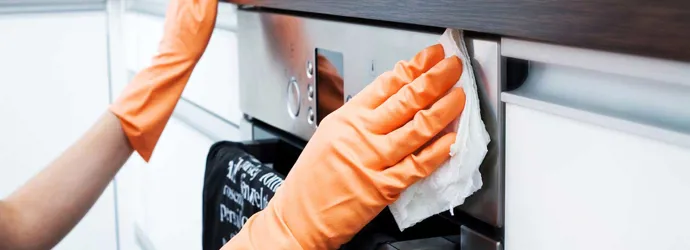 Una persona limpiando el exterior de un horno con un paño y guantes de color naranja
