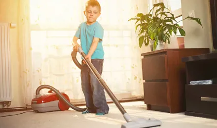 Un chico limpiando la alfombra con una aspiradora