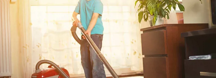 Un chico limpiando la alfombra con una aspiradora