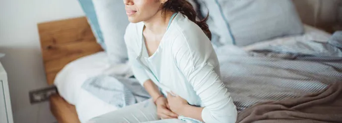 Mujer sentada en la cama con dolor abdominal