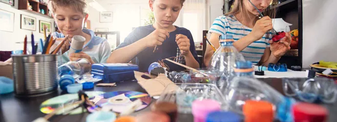 3 niños aprendiendo a reducir los residuos mediante la elaboración de manualidades de plásticos reciclables y tubos de cartón