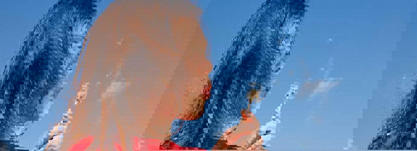 Uma criança pequena que pode precisar de alguns remédios caseiros para a febre dos fenos enquanto sopra um dente-de-leão com um céu azul de fundo