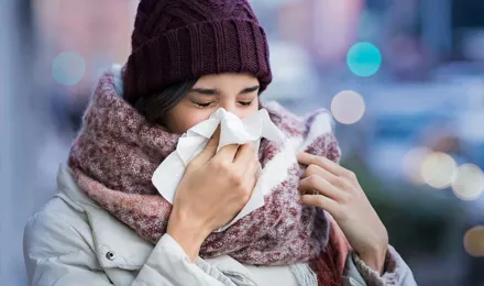 Mulher com roupas de inverno volumosas a sofrer de sintomas de sinusite e a espirrar num lenço de papel ao ar livre