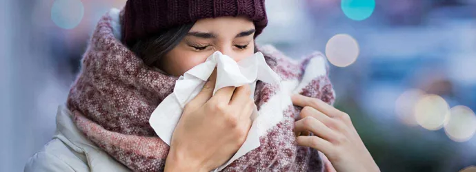 Mulher com roupas de inverno volumosas a sofrer de sintomas de sinusite e a espirrar num lenço de papel ao ar livre