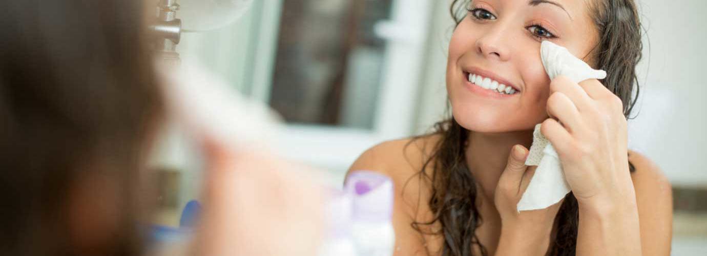 Mulher a sorrir enquanto remove a maquilhagem com um lenço facial