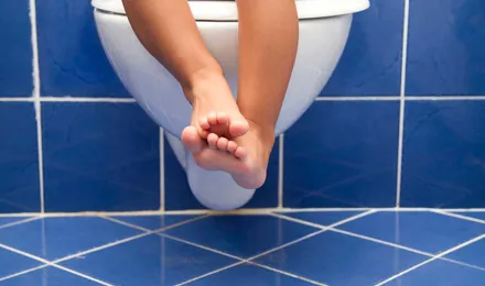 Os pés e pernas de uma criança pendurados numa sanita branca