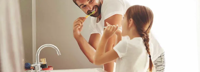 Um homem e a sua filha aprendem a economizar a água enquanto escovam os dentes juntos na casa de banho
