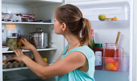 Uma mulher a verificar e limpar o interior de um frigorífico
