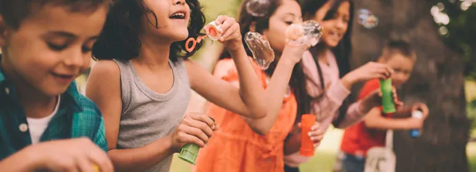 Un grupo de niños de pie sobre una valla de madera haciendo burbujas en verano